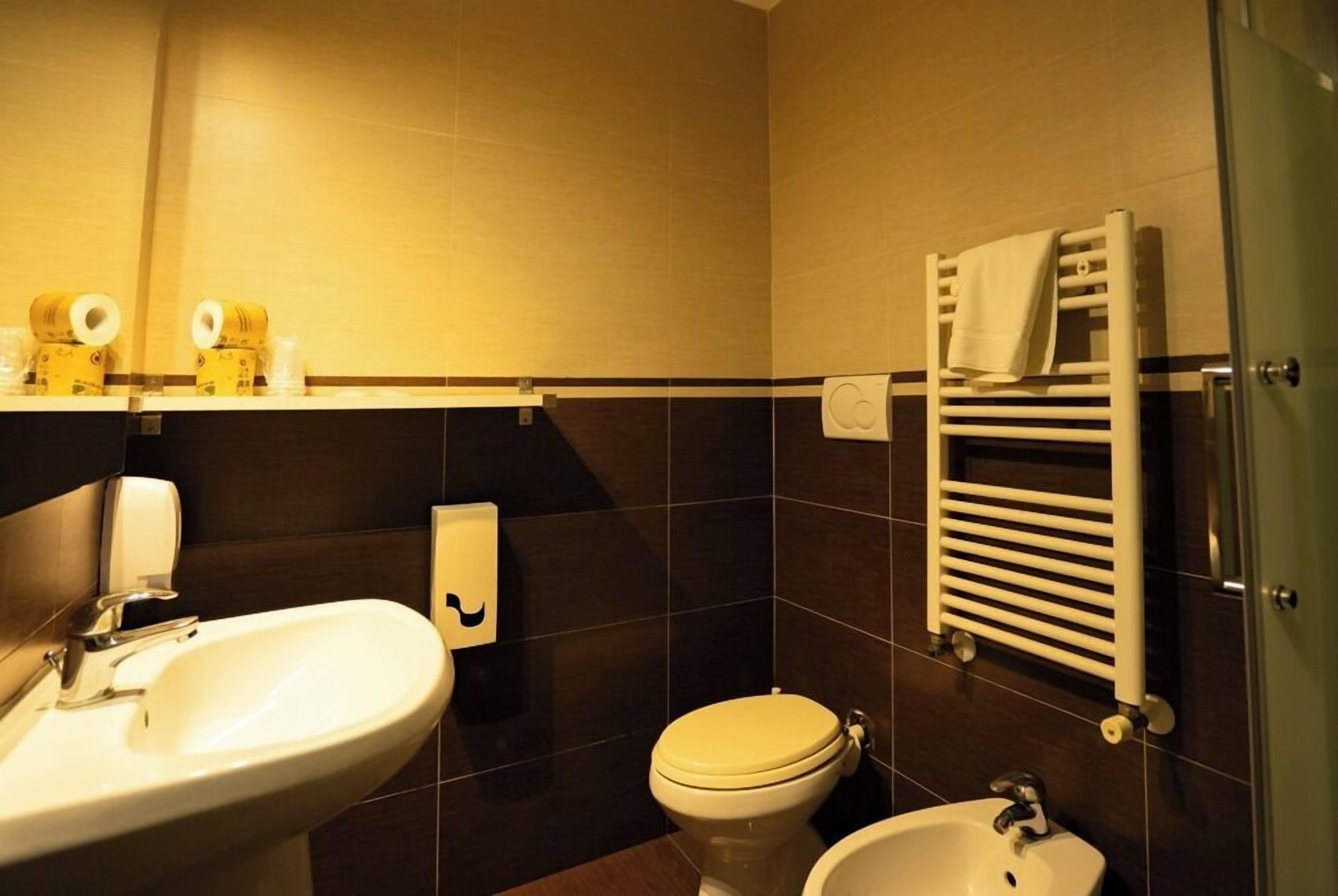 A bathroom with a sink, toilet, and bidet, featuring dark tiles and a towel rack.