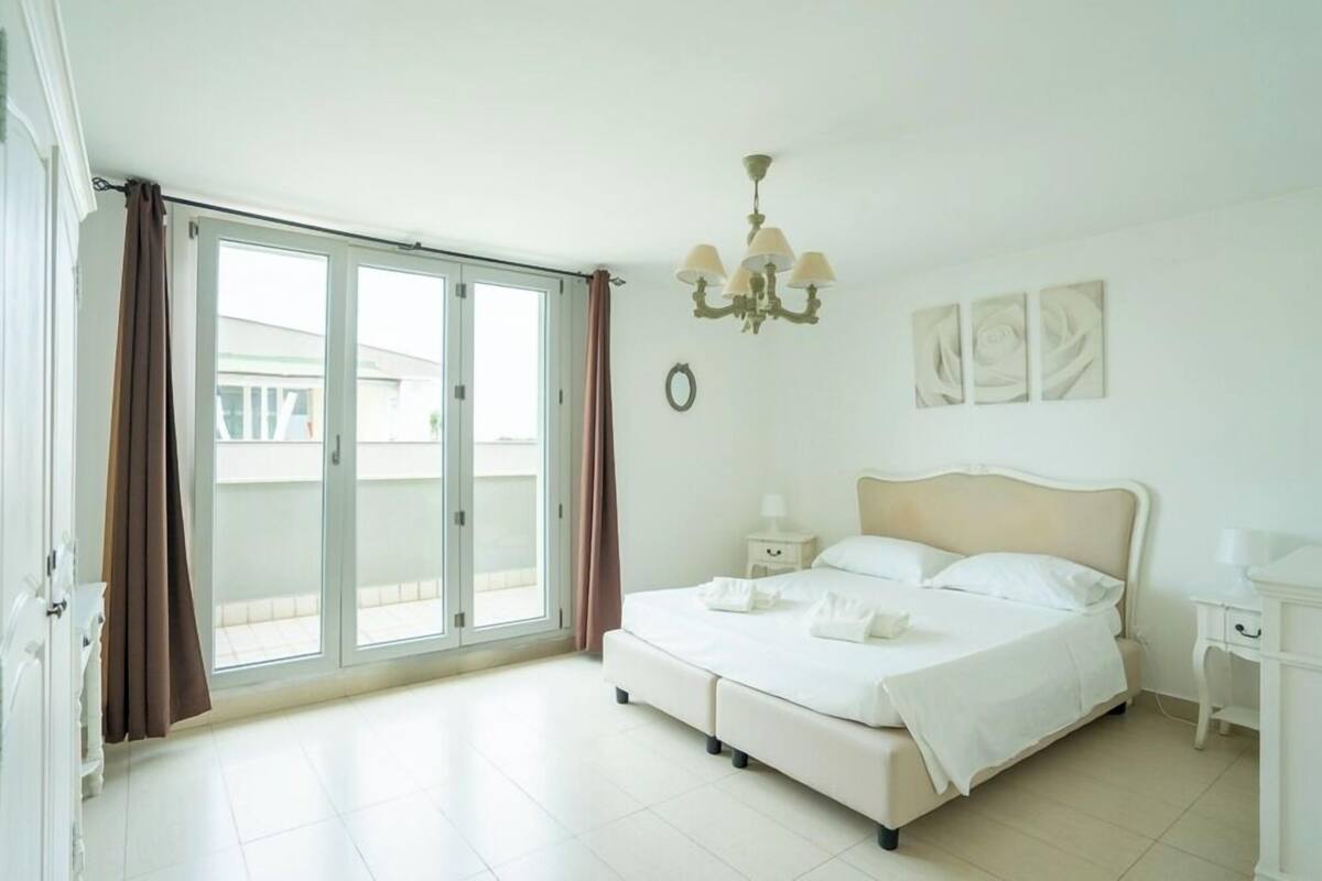 A bedroom with a bed, a nightstand, a chandelier, and a view through a sliding door.
