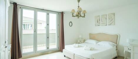 A bedroom with a bed, a nightstand, a chandelier, and a view through a sliding door.