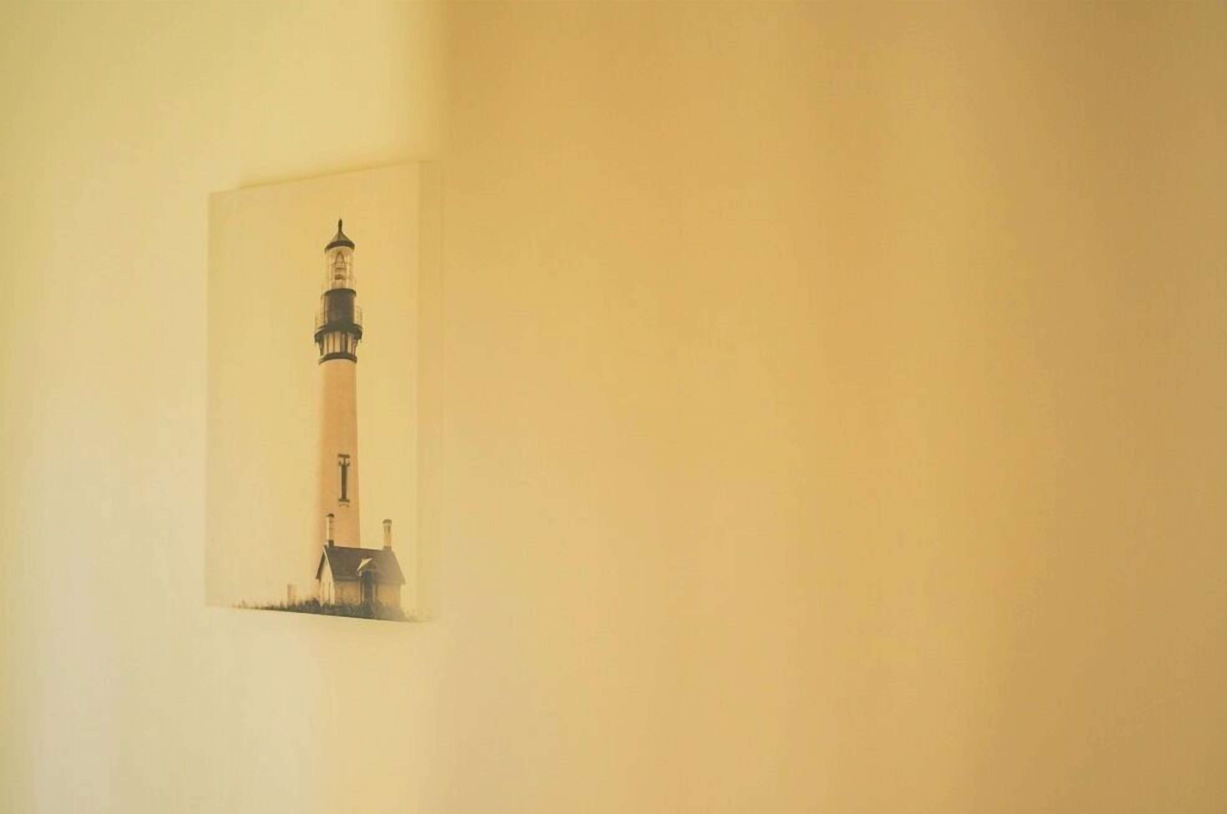 A framed picture of a lighthouse on a plain wall.
