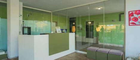 A reception area with a glass partition, a reception desk, and a seating area with cushions.