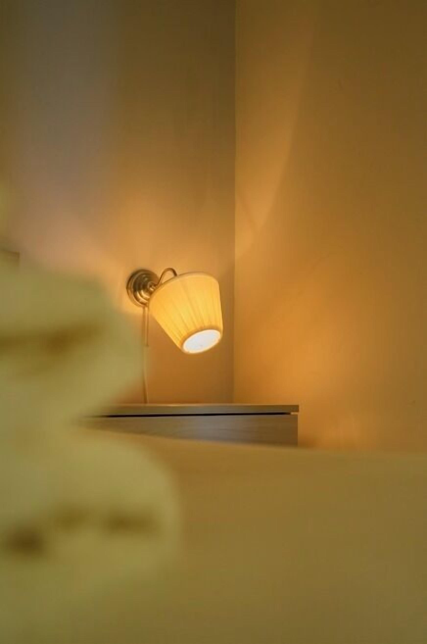 A wall-mounted lamp with a cylindrical shade against a plain wall.
