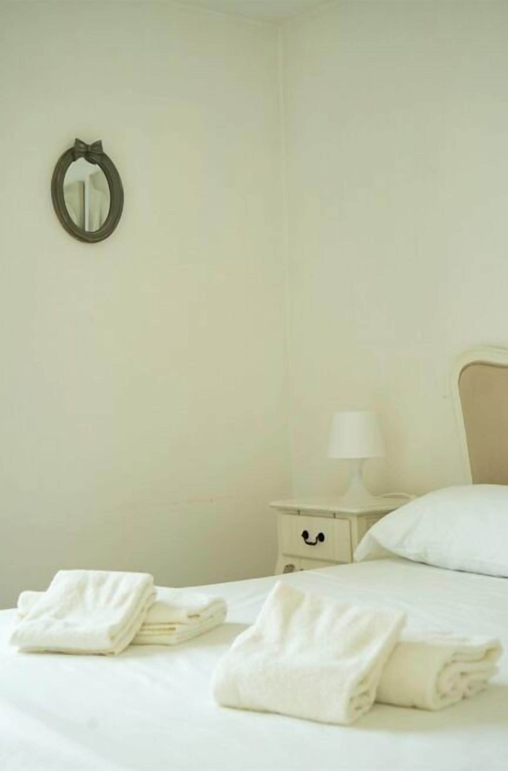 A neatly made bed with folded towels, a bedside table with a lamp, and a wall-mounted mirror.