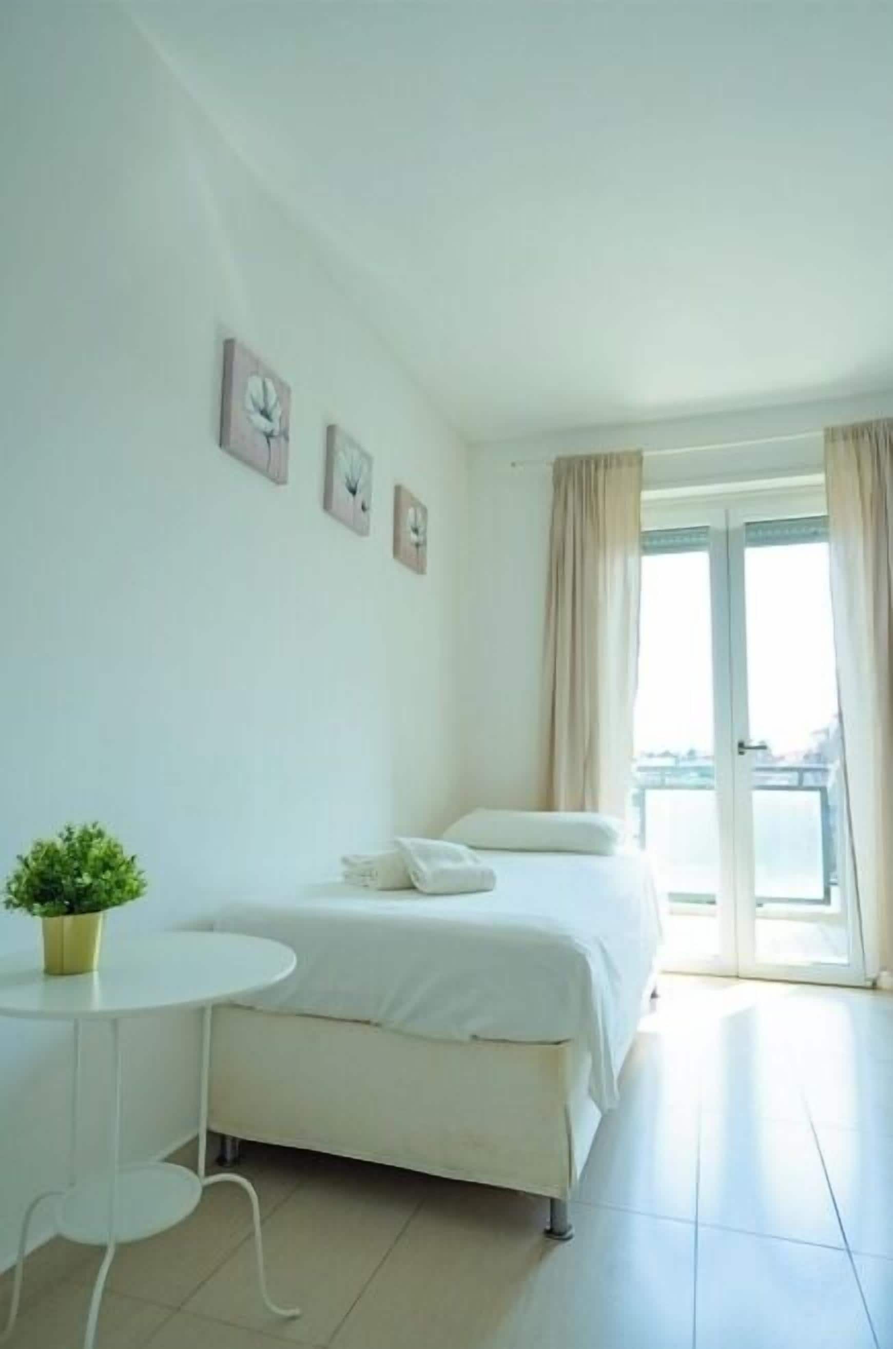 A minimalist hotel room with a bed, a small table, and a potted plant.