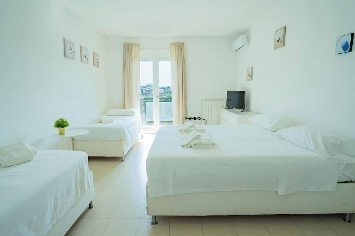 A hotel room with two beds, a small table with a plant, a TV, and a balcony with curtains.