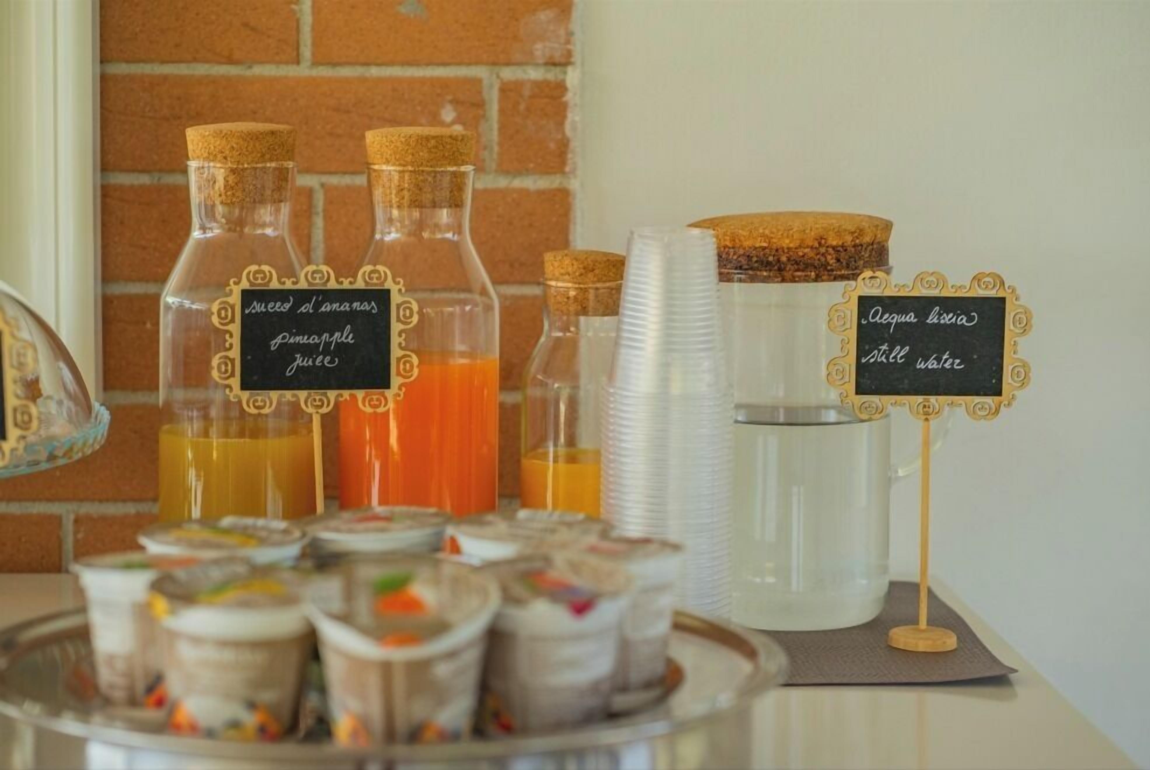 A beverage station with labeled bottles of pineapple juice and still water, and a tray of assorted food items.