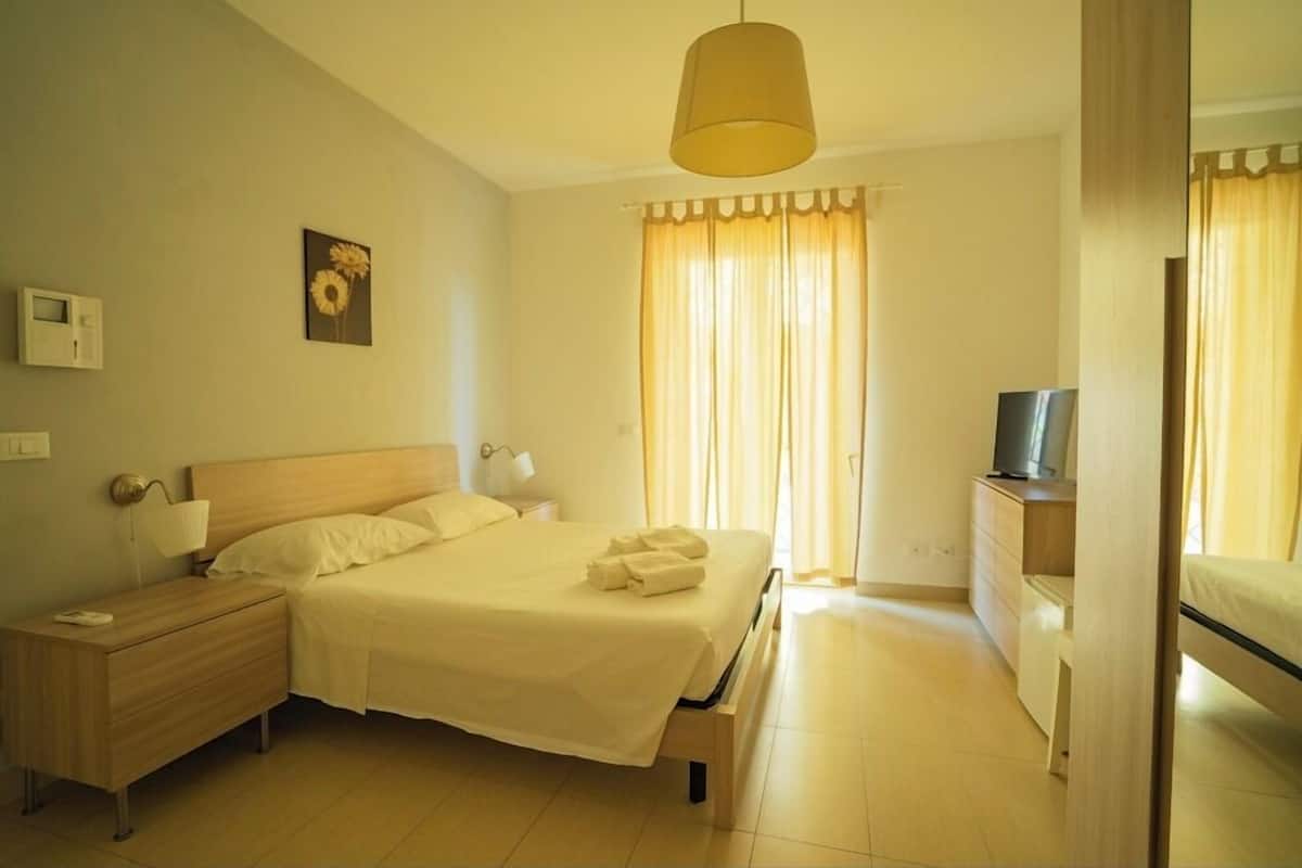 A hotel room with a bed, bedside table, lamp, TV, and curtains.