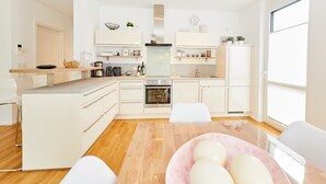 A modern kitchen with white cabinetry, a wooden dining table, and a large window providing natural light. - Auszeit (Bernkastel-Kues)