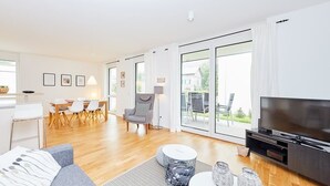 A modern living room with a grey sofa, a round coffee table, and a TV. There is a dining area with a table and chairs in the background. - Auszeit (Bernkastel-Kues)