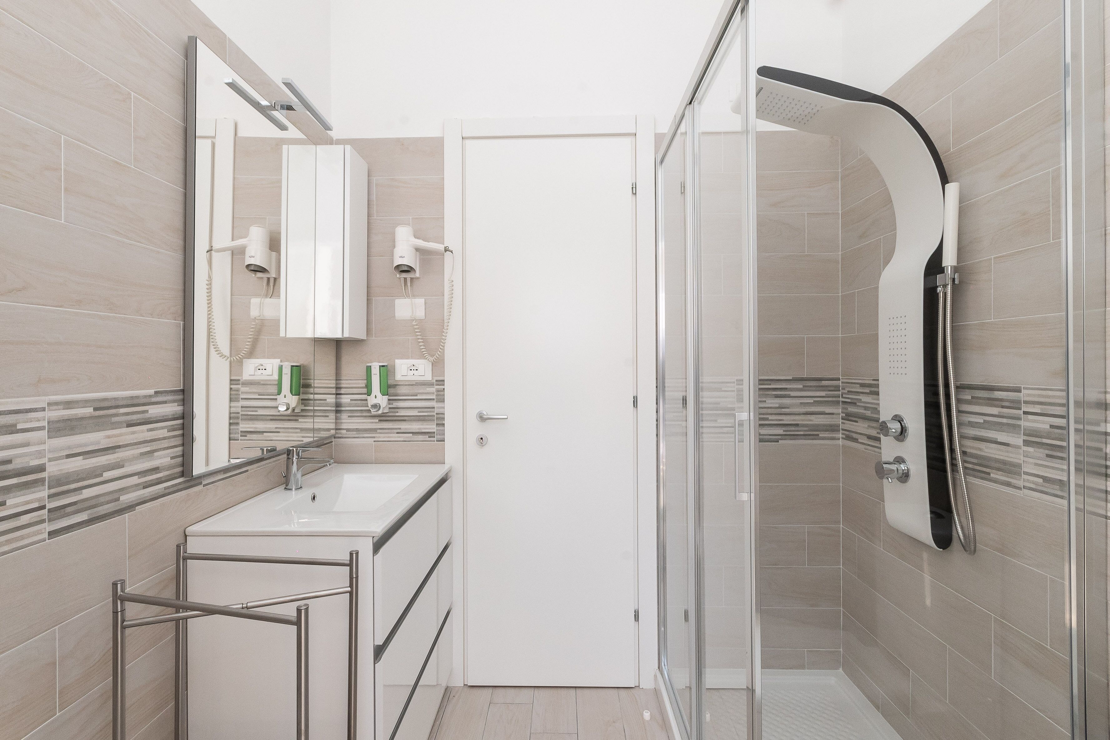 Une salle de bain moderne avec une douche à parois de verre, un lavabo blanc et un miroir doté de sèche-cheveux intégrés.
