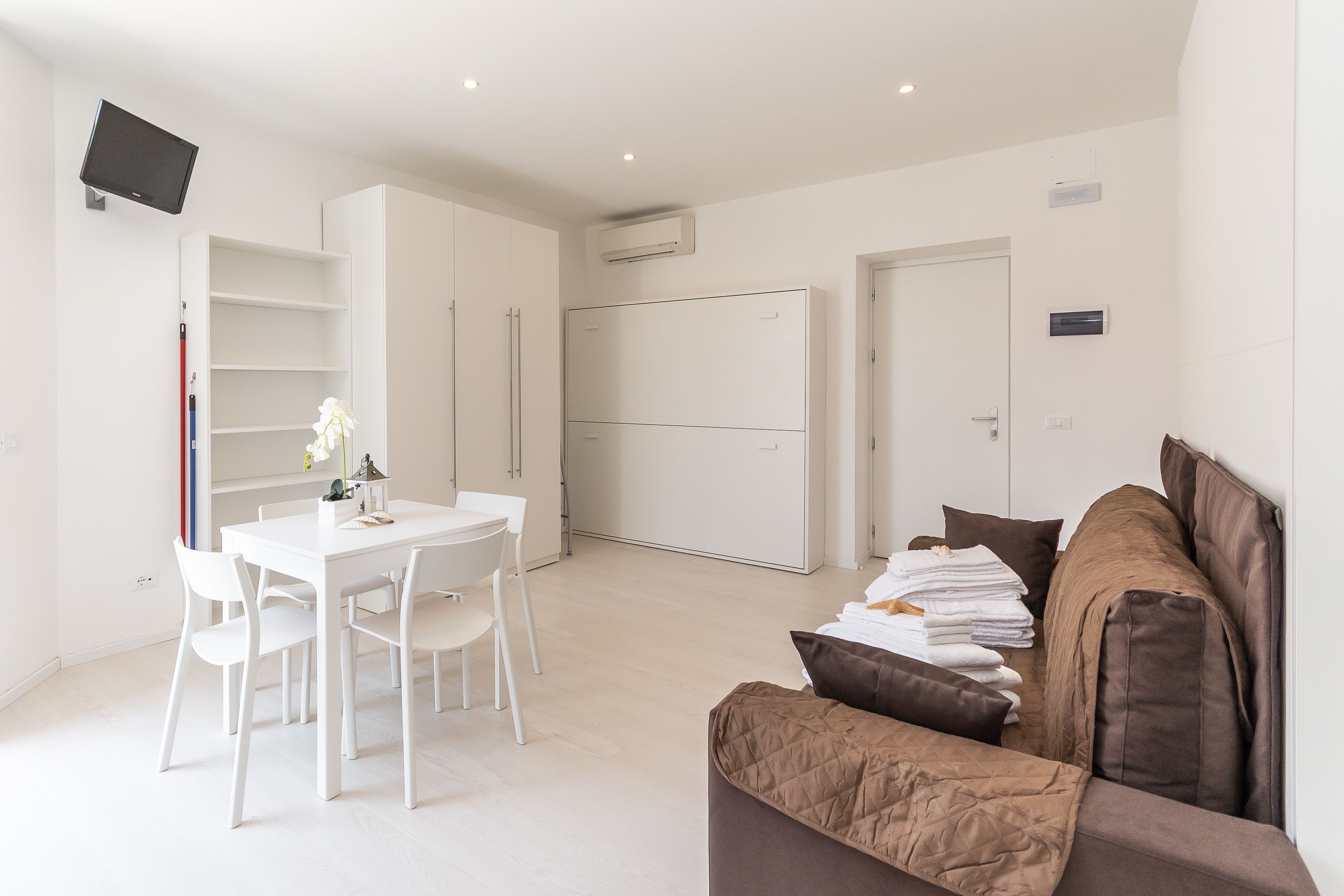 Ein modernes, helles Zimmer mit Essbereich, einer Couch und einem an der Wand befestigten Fernseher.