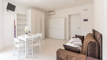 A modern, well-lit room with a dining area, a sofa, and a TV mounted on the wall.