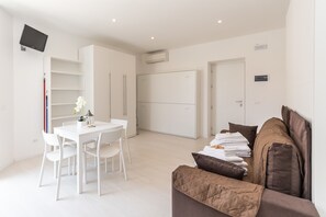 A modern, well-lit room with a dining area, a sofa, and a TV mounted on the wall. - Residence Bike and Beach (Finale Ligure)