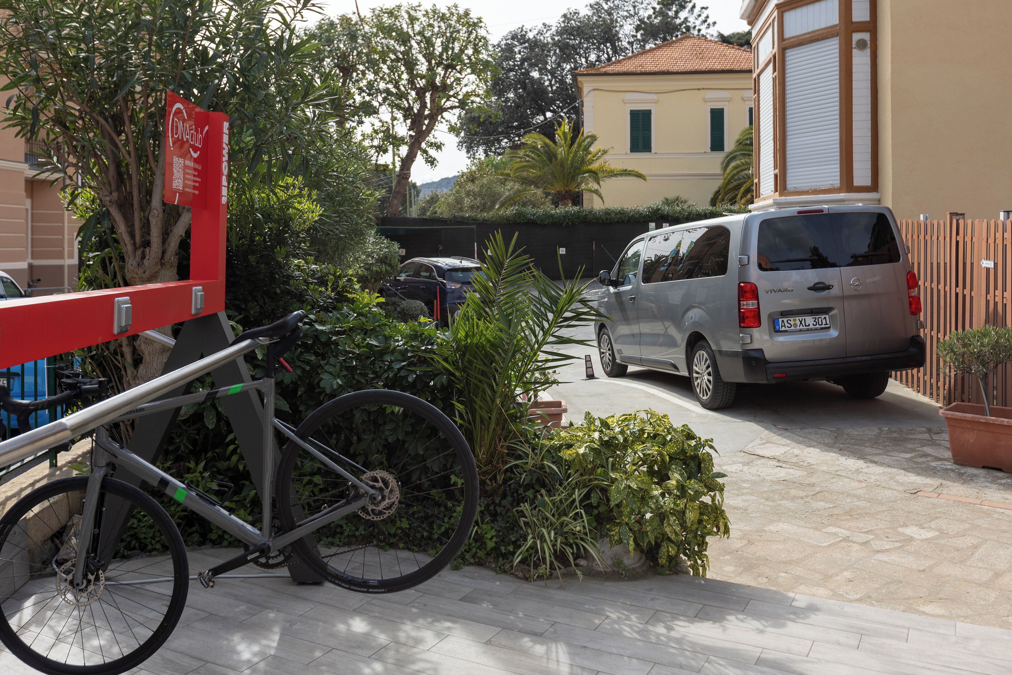 Una bicicleta estacionada en un barrio residencial, con una furgoneta y un edificio al fondo.