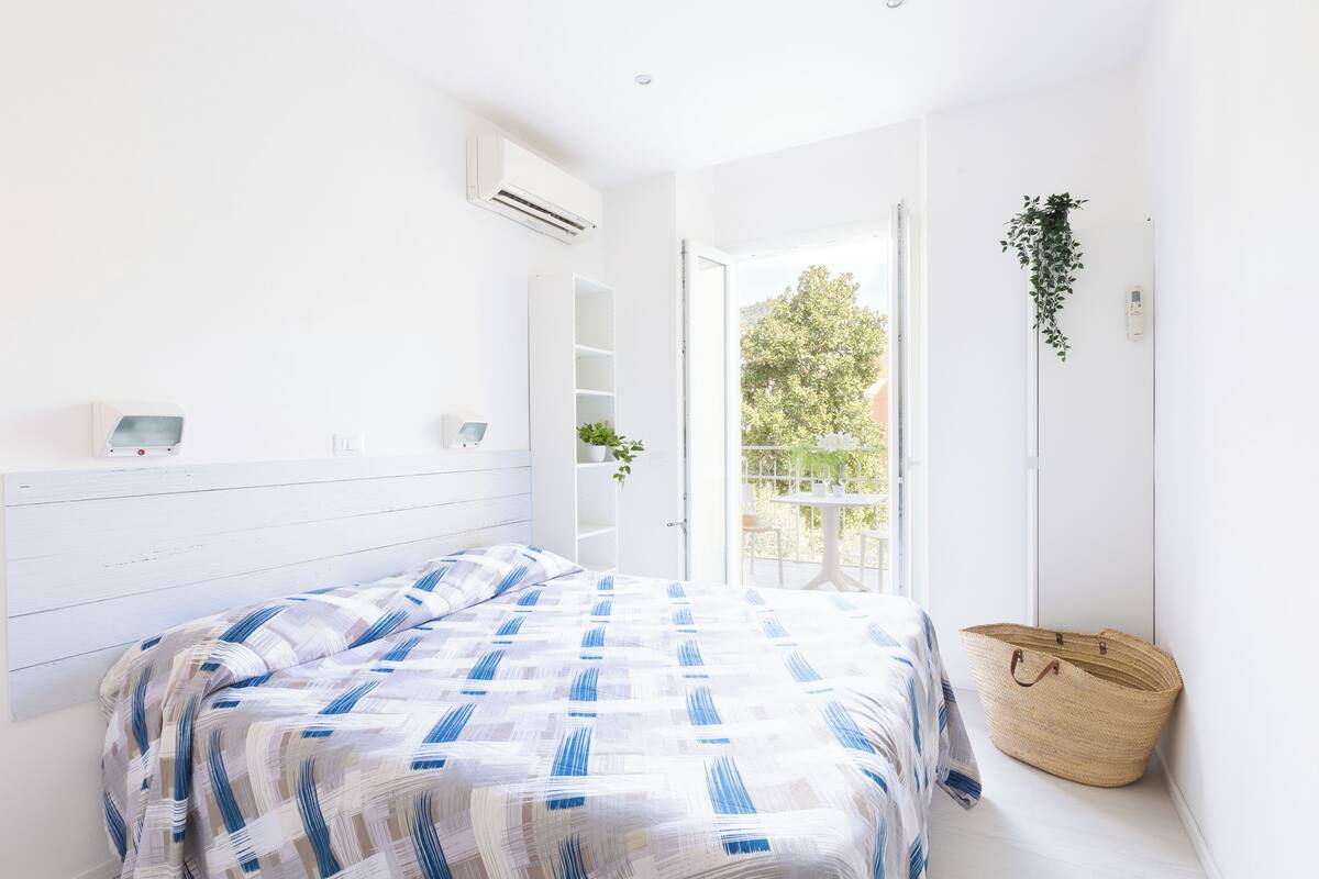 Una camera da letto con un letto, un comodino, una pianta pensile e una finestra vista verde.