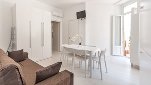 A modern, well-lit living area with a white dining table, chairs, and a sofa with brown cushions.