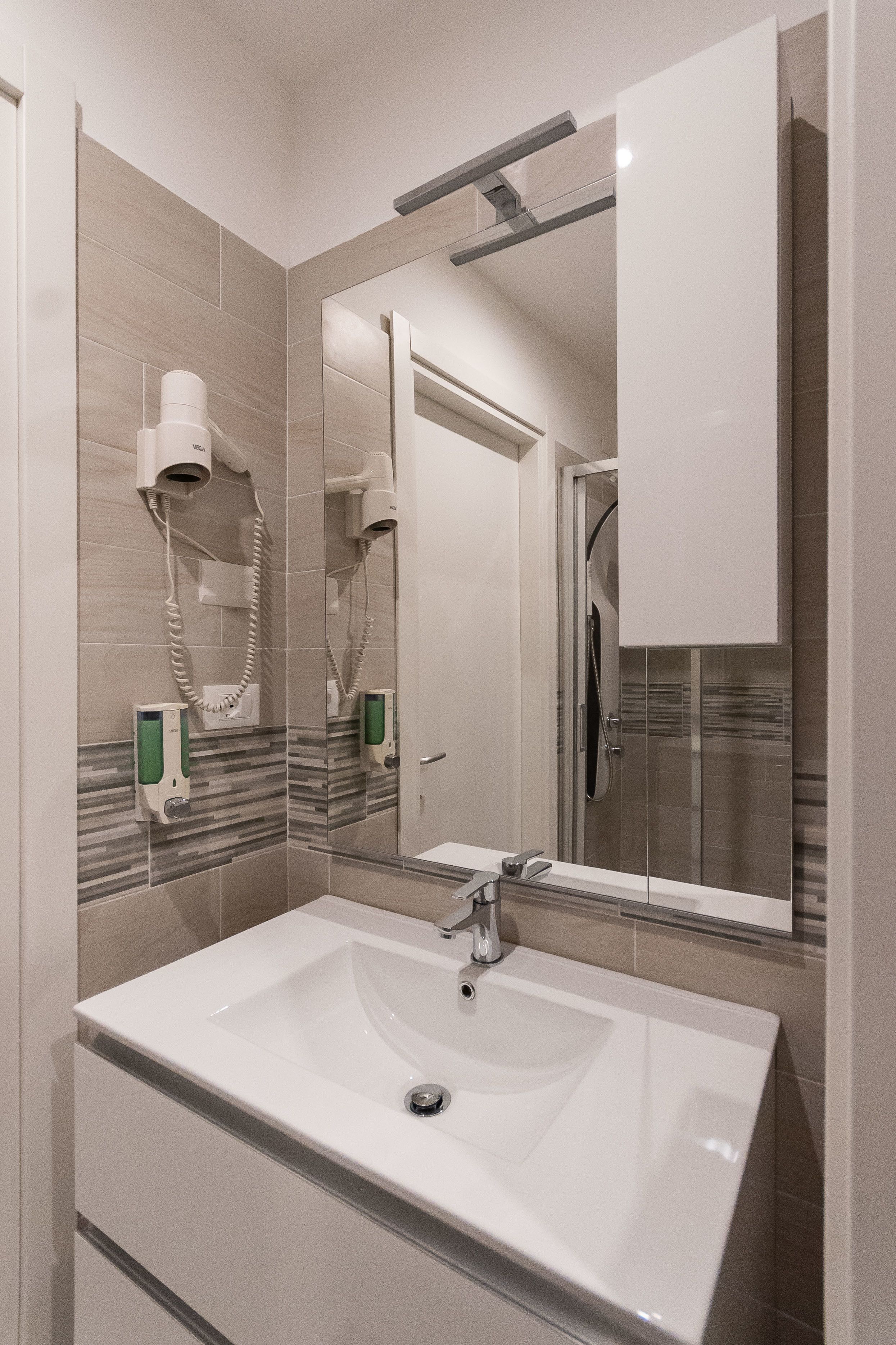 A modern bathroom with a large sink, a mirror, and hair dryers mounted on the wall.