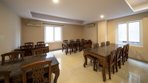 Un vaste espace dédié à la salle à manger, avec une grande table et des chaises en bois, des unités de climatisation fixées aux murs et de grandes fenêtres laissant entrer la lumière naturelle.