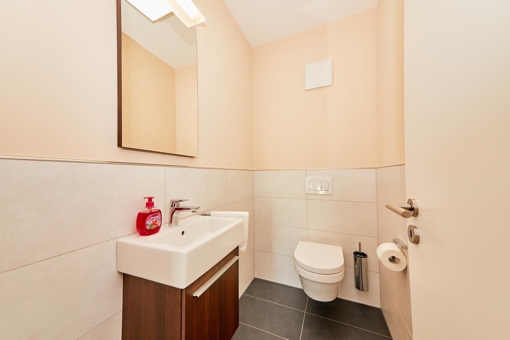 A bathroom with a white sink, a mirror, a toilet, and a trash bin.