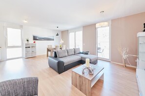 Ein modernes Wohnzimmer mit einer Eckcouch, einem Couchtisch und einem Essbereich mit Tisch und Stühlen.