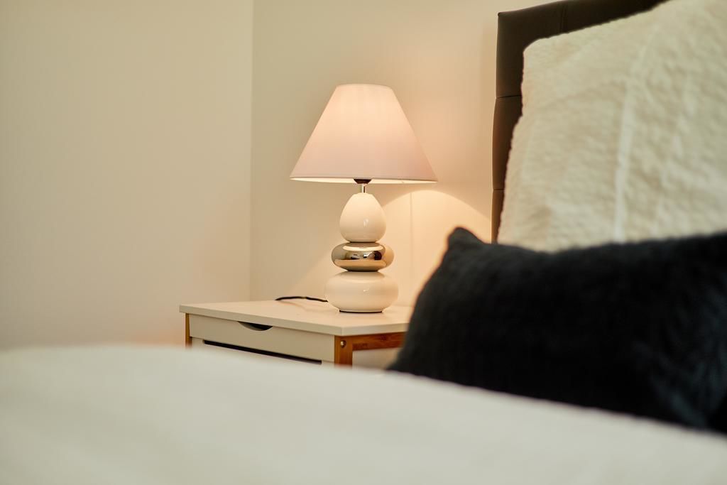 Un lit avec un oreiller blanc et un oreiller noir, une table de chevet avec une lampe, et un mur orné d’un motif texturé.