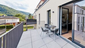 Een modern balkon met een tafel, stoelen en een glazen deur naar een kamer, met uitzicht op een heuvel.