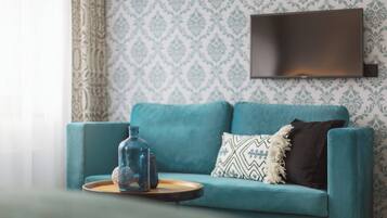 A teal sofa with patterned cushions, a clear glass bottle, and a tray on a wooden table.