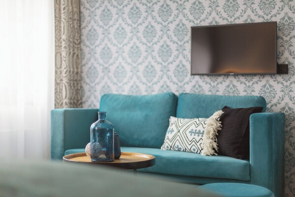 A teal sofa with patterned cushions, a clear glass bottle, and a tray on a wooden table.