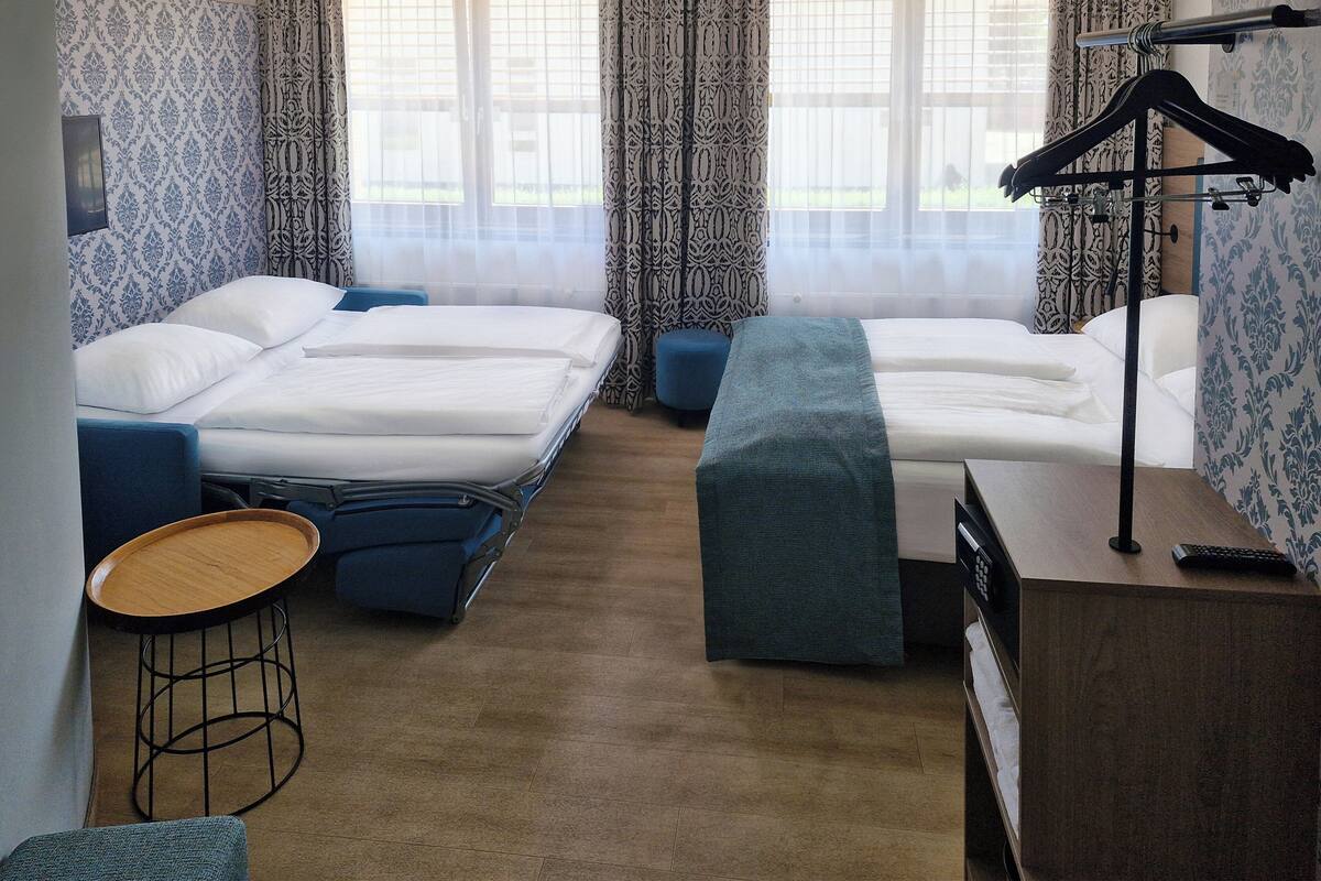 Hotellihuone, jossa on kaksi sänkyä, pieni pyöreä pöytä, penkki ja vaatekaappi.