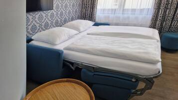 A hospital room with a bed, a wooden chair, patterned wallpaper, and curtains.