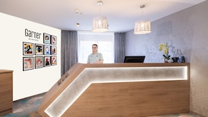 A hotel reception area with a modern design, including a wooden reception desk with integrated lighting, a wall-mounted art display, and a large window providing natural light.