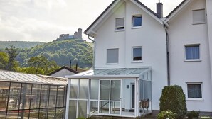 A modern two-story house with a glass conservatory, a small garden, and a view of a castle on a hill. - Bella Vista (Bernkastel-Kues)