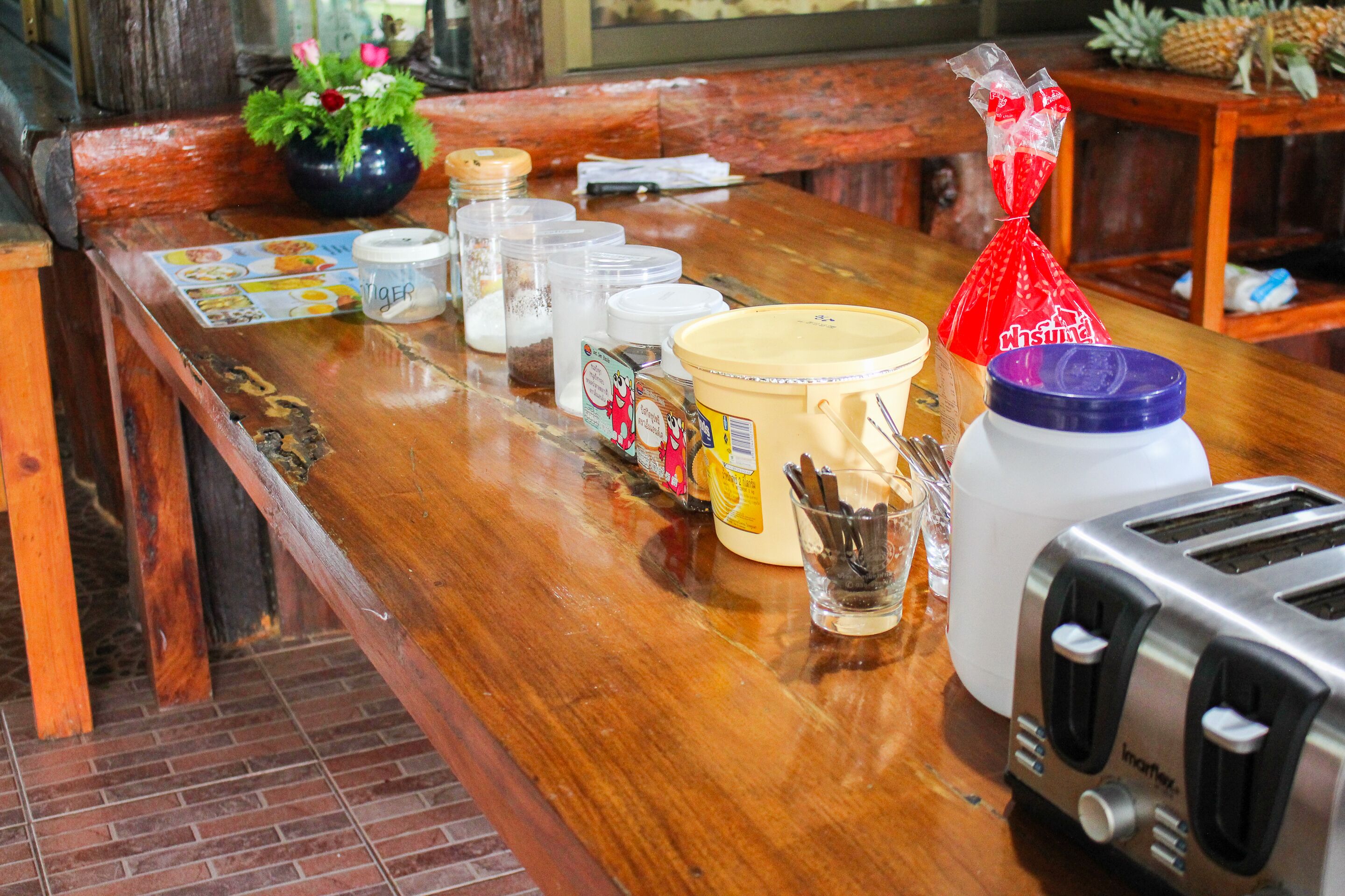 A wooden bar counter with various food items and condiments, a toaster, and a potted plant.