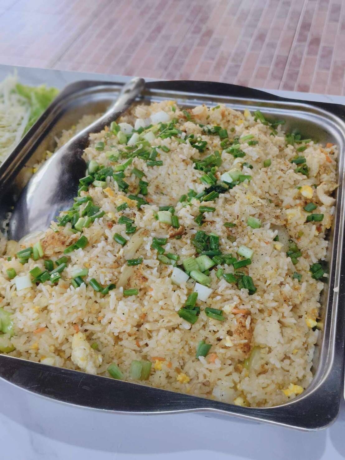 A stainless steel serving dish filled with fried rice garnished with chopped green onions.