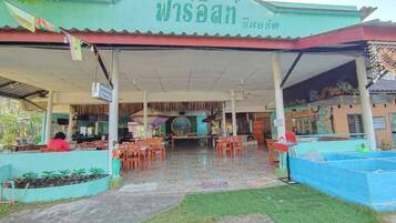 Un restaurante con zona de estar al aire libre cubierta, un letrero y piso de baldosas.