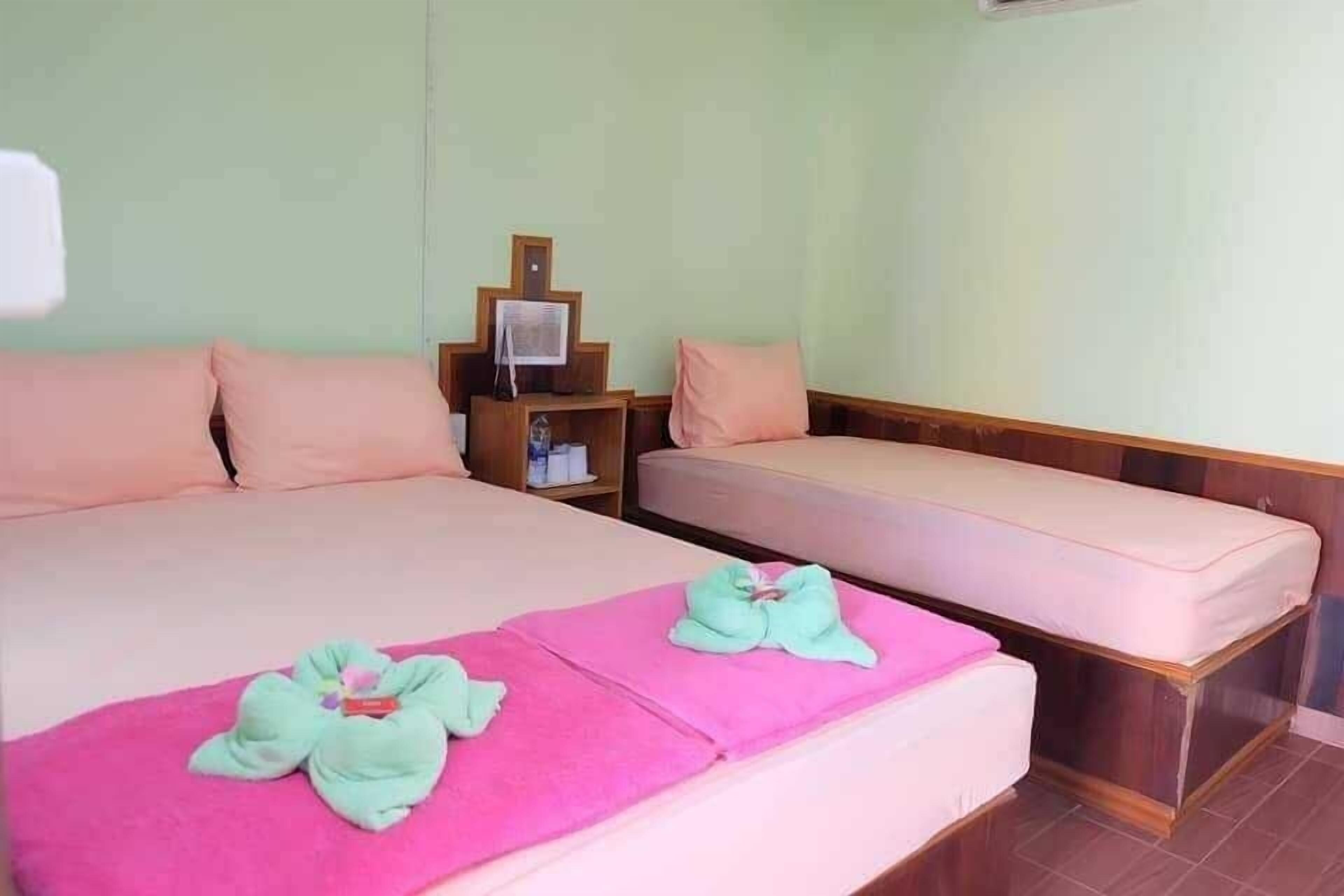 A hotel room with a large bed, a smaller bed, a wooden nightstand, and a small table with a fan.