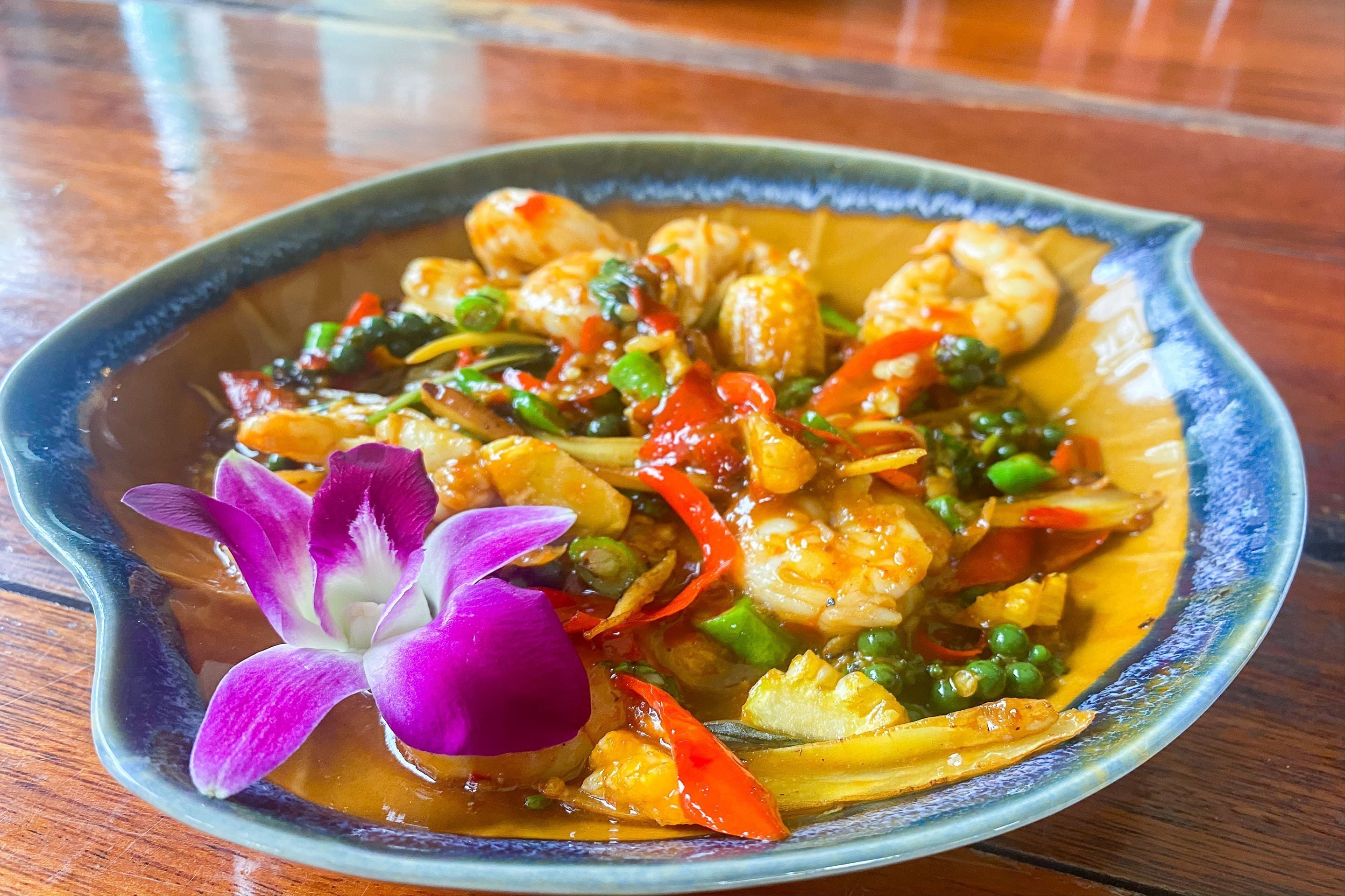 A bowl of seafood curry with vegetables and a purple flower garnish.