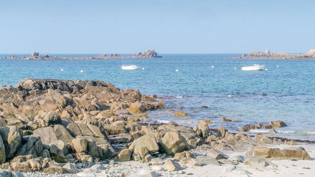 Une côte rocheuse bordée de bateaux sur l’eau.