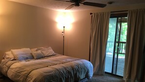 Un dormitorio con una cama, una lámpara de pie y vistas al exterior a través de un ventanal corredero.