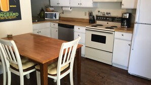 Una cocina con armarios blancos, una mesa de madera y sillas blancas.