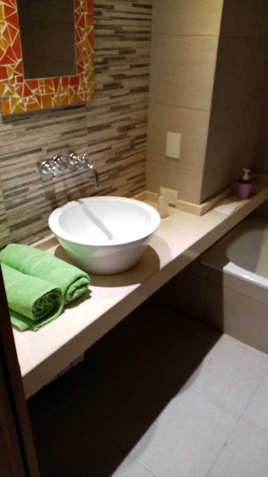 Un bagno con un lavandino bianco, un asciugamano verde e uno specchio con pannelli decorativi geometrici.