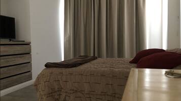 A bedroom with a bed, a wooden dresser, a television on the dresser, and a window with curtains.