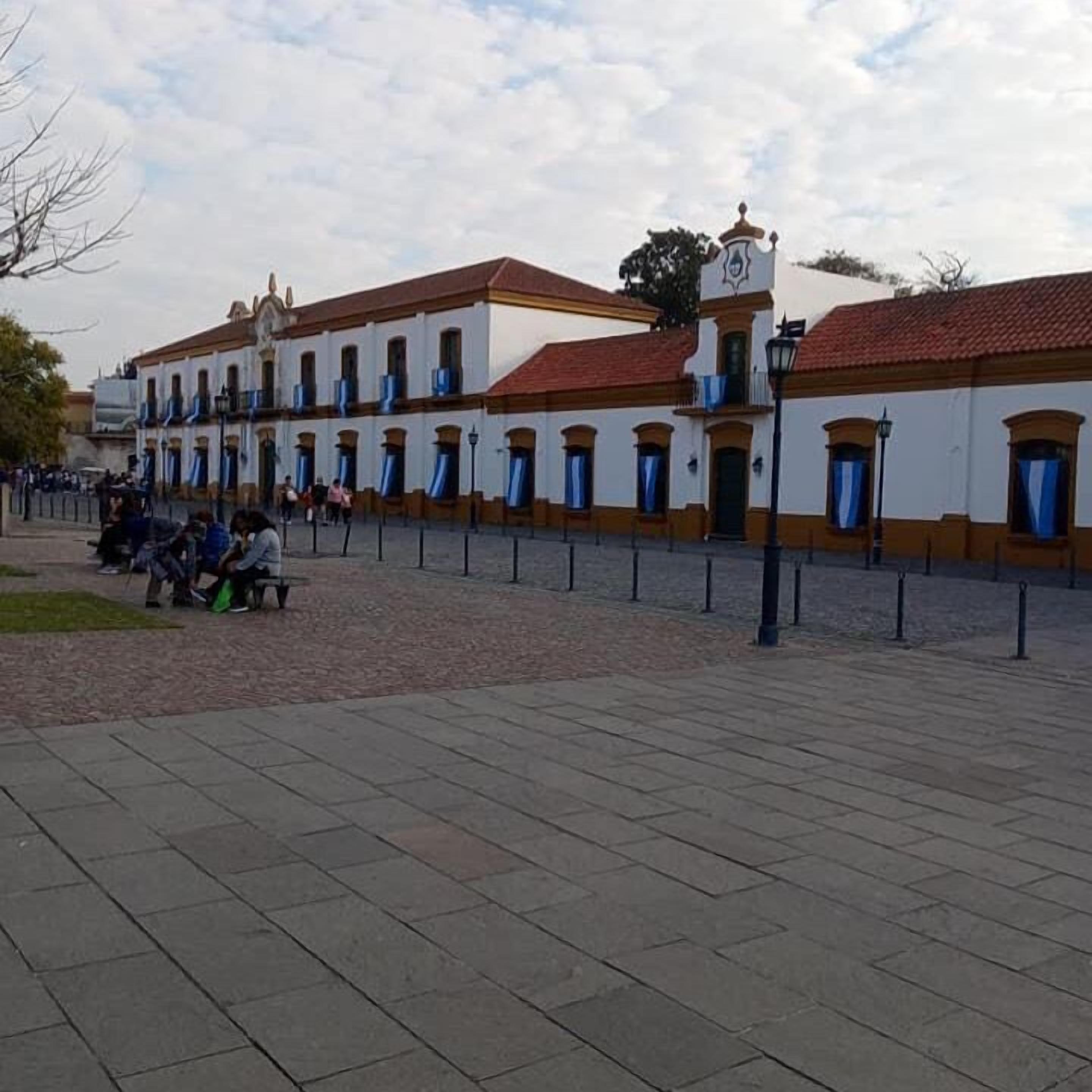 A building with a symmetrical facade, multiple windows with blue shutters, and a central entrance with a sign.