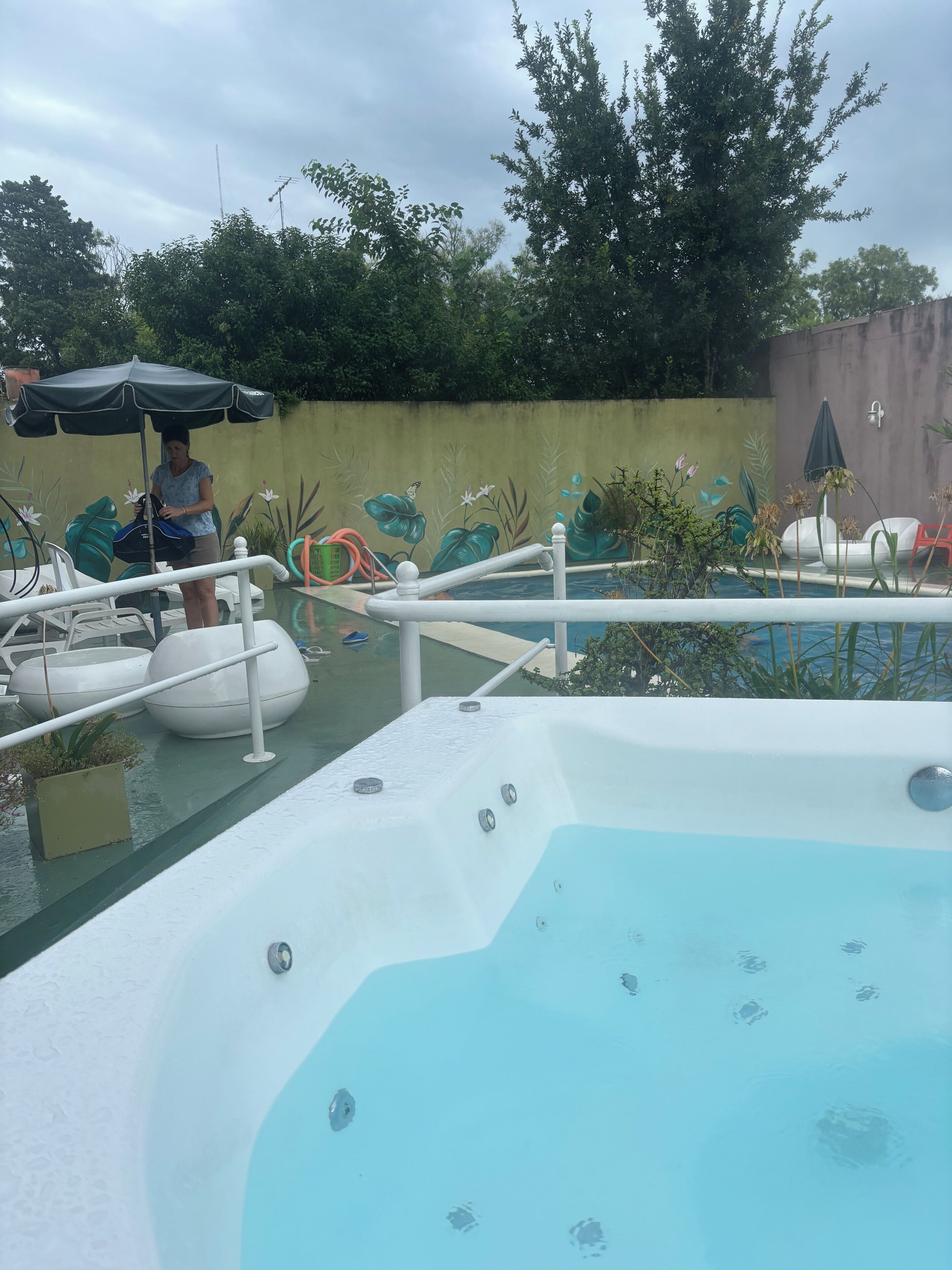 Zona de piscina con jacuzzi, sillas de descanso y un mural en la pared.