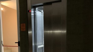 An elevator with a metallic finish, a glass door, and a visible emergency exit sign. - Lujan Homes Apart Hotel (Luján)