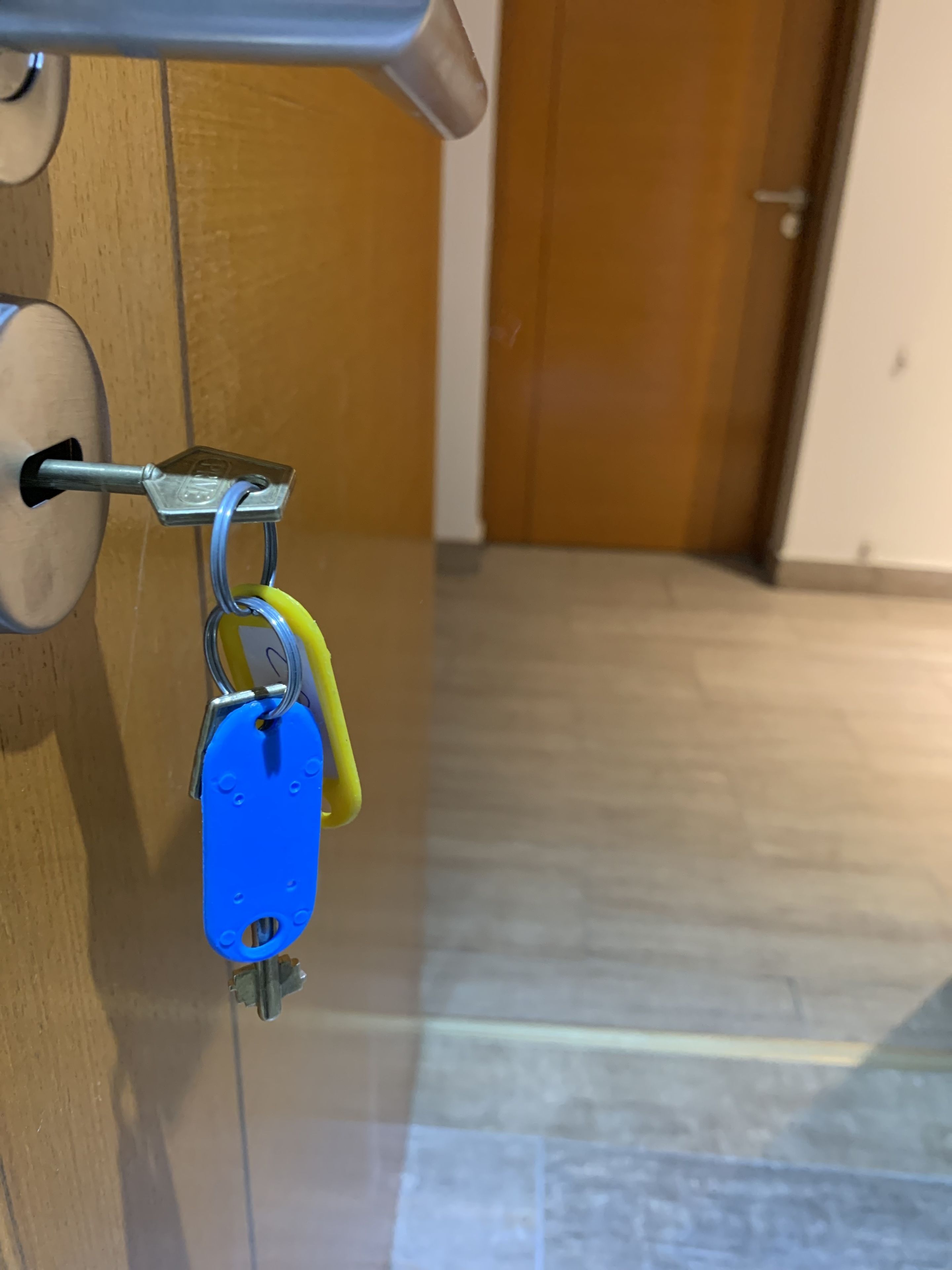 A keychain with a blue key and a yellow key attached to a metal keyring, hanging from a door lock.