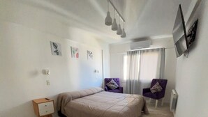 A bedroom with a bed, a nightstand, a chair, and a window with curtains. - Lujan Homes Apart Hotel (Luján)