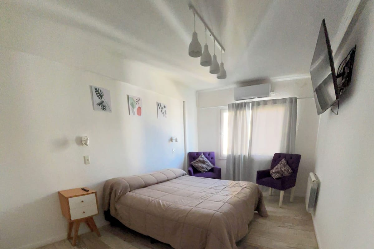 Une chambre à coucher avec un lit, une table de chevet, une chaise et une fenêtre avec des rideaux.