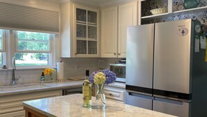 A modern kitchen with white cabinets, a marble countertop, and a stainless steel refrigerator. - Perfect Maine Getaway – Walk to Downtown, Cozy for All - Flexible Cancellation. (Kennebunk)