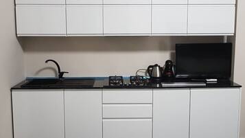 A modern kitchen with white cabinets, a black countertop, a gas stove, a kettle, and a television.